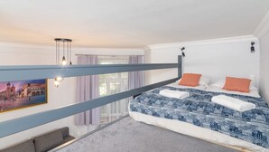 Une chambre avec un lit superposé, une vue sur le paysage urbain par la fenêtre, un canapé gris et un tableau au mur.