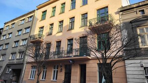 Un immeuble à plusieurs étages, doté d’une façade beige, de nombreuses fenêtres à encadrements verts et de balcons avec des garde-corps en métal.