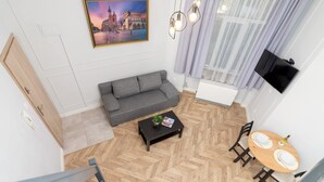 Un salon moderne avec un canapé gris, un parquet en bois disposé en chevrons, une table basse avec un magazine et un coin repas comprenant une table et des chaises.
