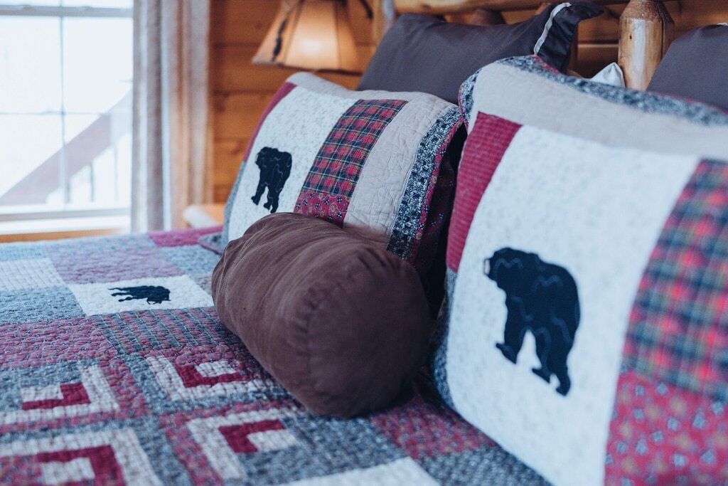 Een knus ingerichte kamer met een gewatteerde plaid met berenmotieven en een bruin kussen.