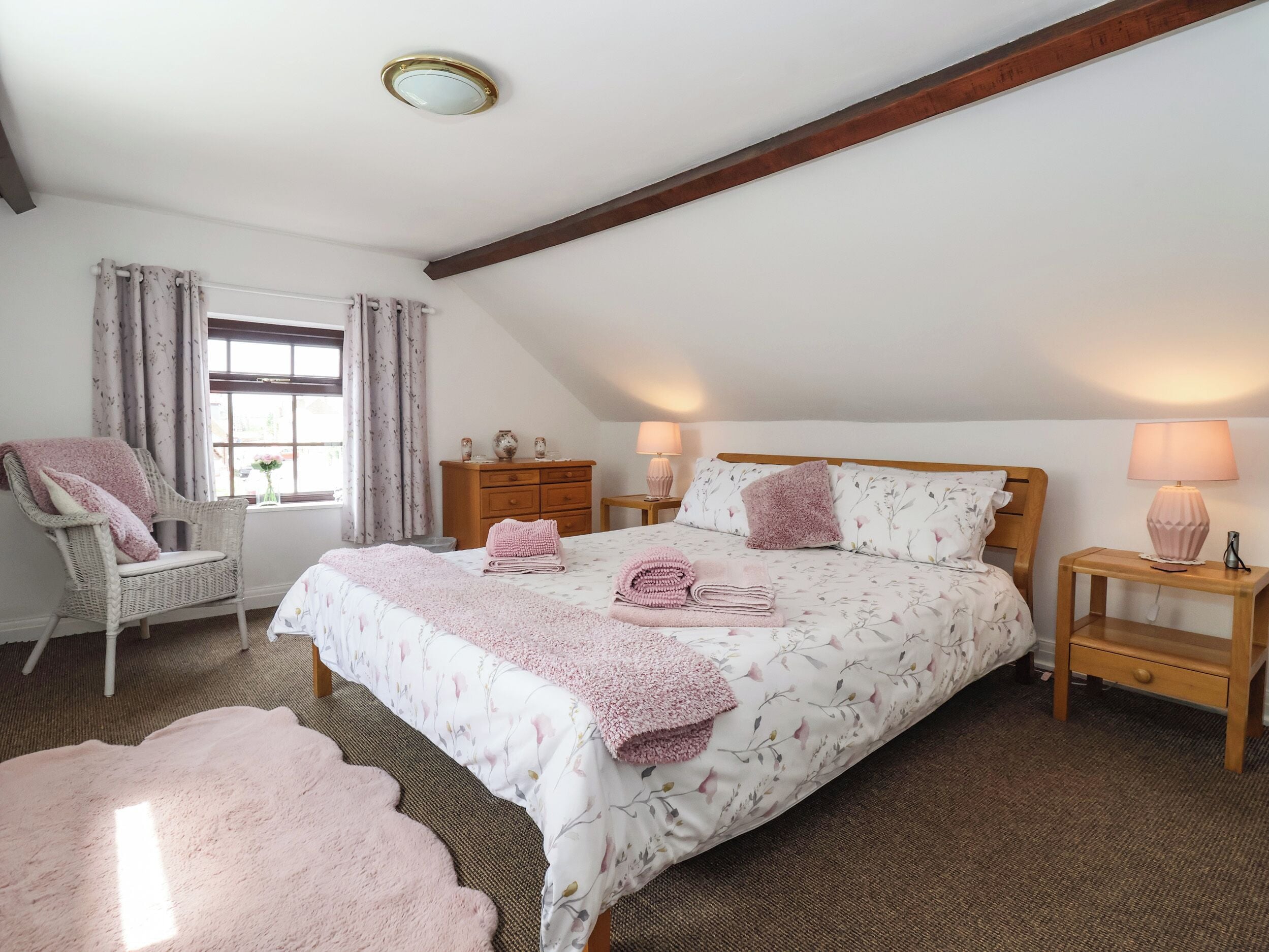 Une chambre à coucher avec un grand lit, deux tables de chevet, une chaise, une commode et une fenêtre avec des rideaux.