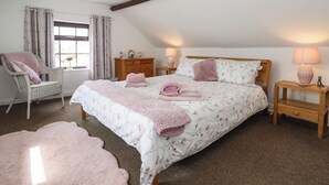A bedroom with a large bed, two bedside tables, a chair, a dresser, and a window with curtains.