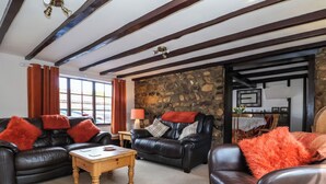 A cozy living room with leather sofas, a wooden coffee table, and a stone wall.