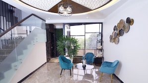 A modern interior with a glass staircase, a seating area with two chairs, a coffee table, and a decorative wall piece. - DD Suites (Agra)