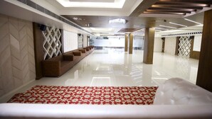 A spacious lobby with a modern design, featuring a patterned red carpet, a seating area with brown sofas, and a bright, well-lit ceiling with recessed lighting. - DD Suites (Agra)