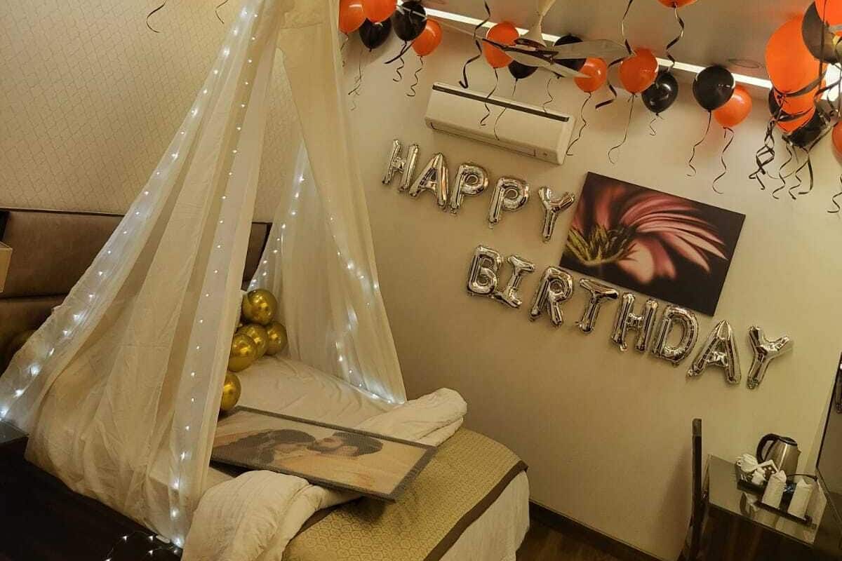 A bedroom with a canopy bed, a wall-mounted air conditioner, and a 'Happy Birthday' balloon decoration.