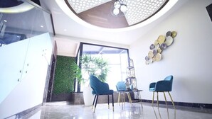 A modern lobby with a glass partition, a green wall with plants, and two blue chairs. - DD Suites (Agra)