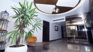 A modern interior with a large potted plant, a wooden ceiling, and a reflective wall. - DD Suites (Agra)