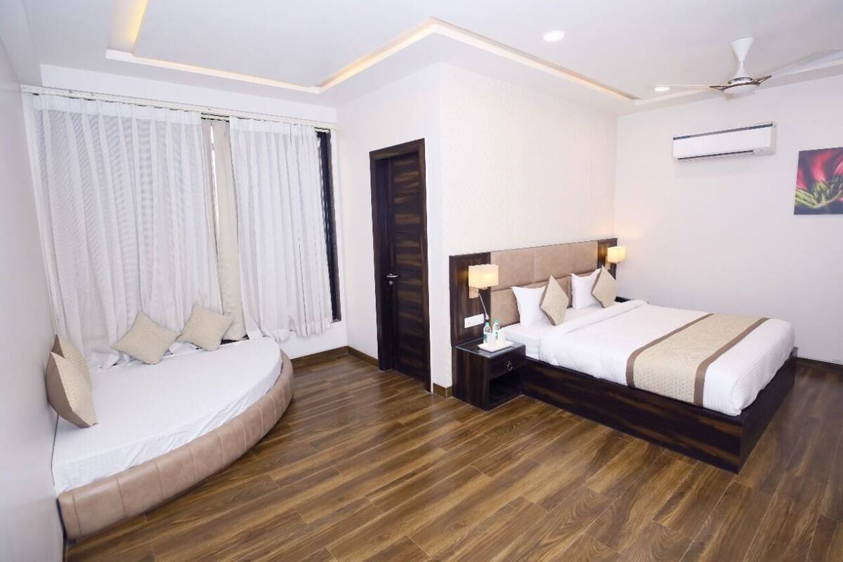 A hotel room with a large bed, a sofa bed, a nightstand, and an air conditioning unit.