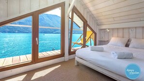A bedroom with a large window overlooking a body of water and a mountain.