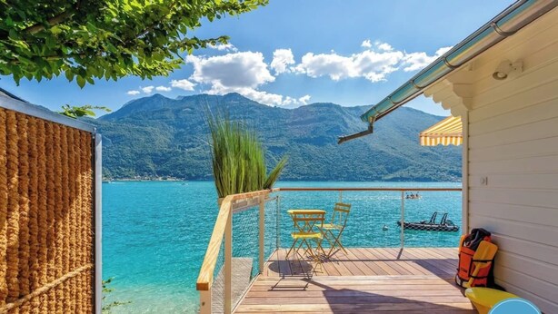 A wooden deck with a view of a lake and mountains, a table and chairs, and a life jacket on the right.