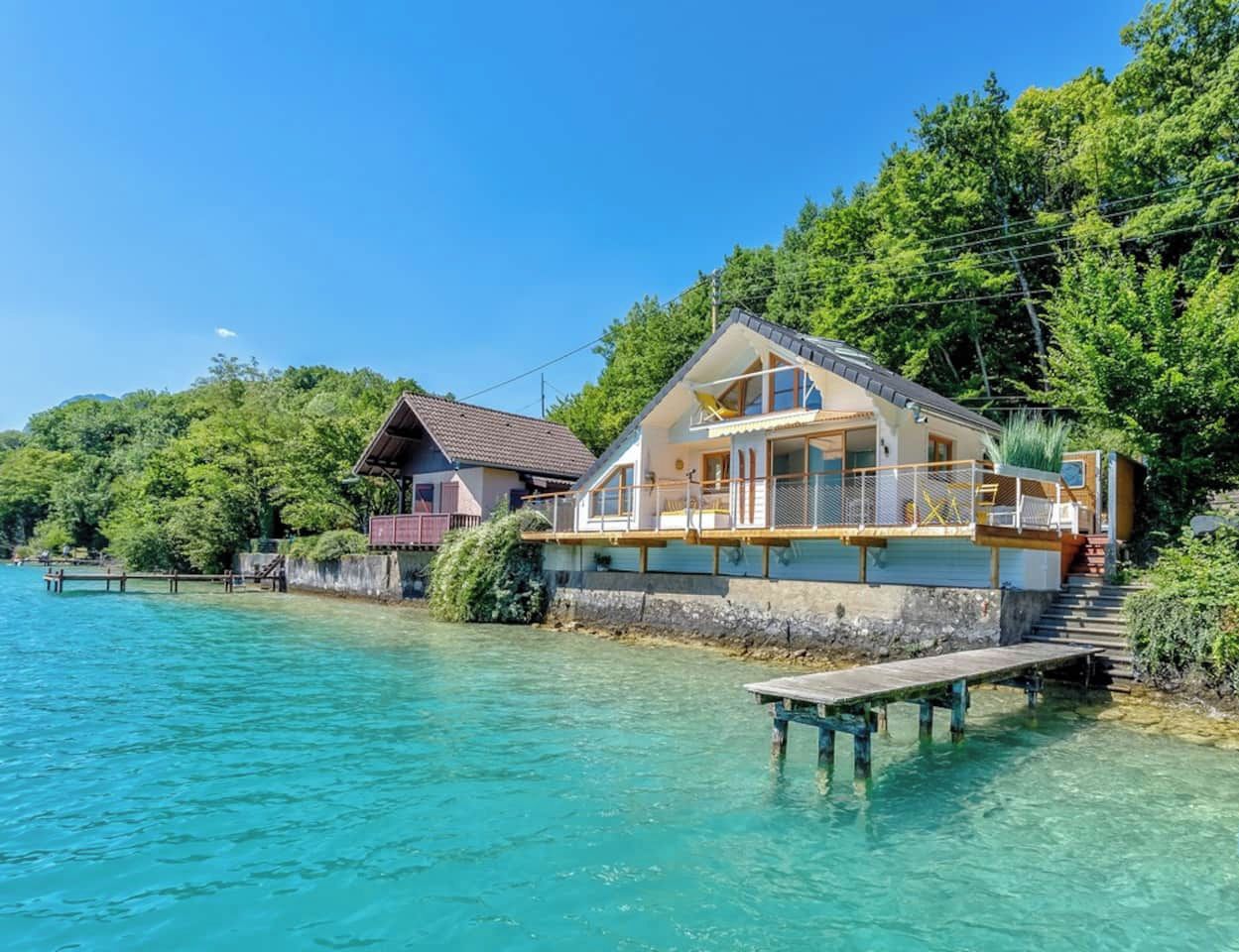 Une propriété située au bord de l’eau, avec une grande maison dotée d’un balcon, d’un quai et d’une terrasse en bois.