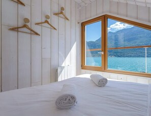 A bedroom with a bed, a window with a view of a lake and mountains, wooden wall panels, and a towel on the bed.