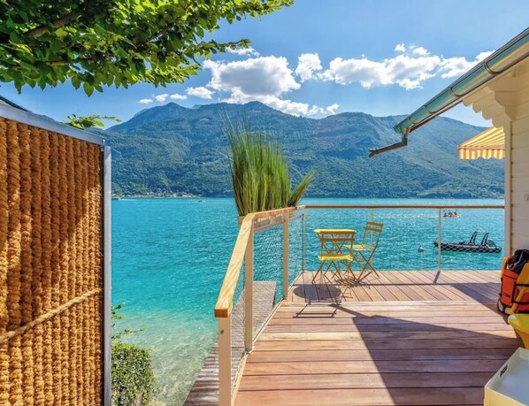 A wooden deck with a view of a lake and mountains, a table and chairs, and a life jacket on the right.