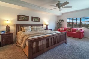 A bedroom with a large bed, two bedside tables with lamps, a red sofa, and a ceiling fan.