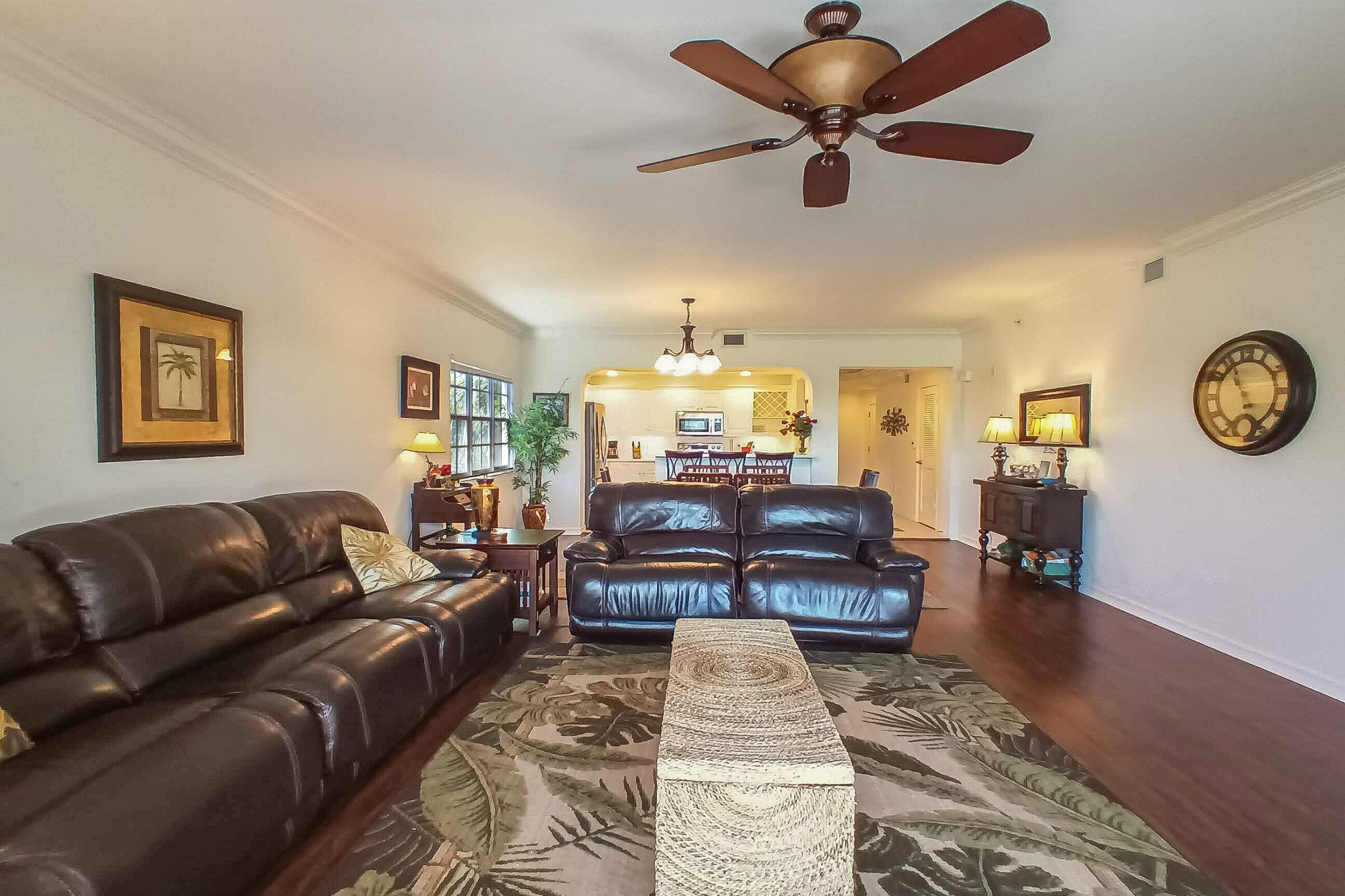A living room with a ceiling fan, two leather sofas, a coffee table, and a dining area in the background.