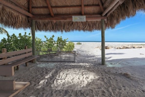 Een strandhut met rieten dak, een houten bank en een bordje dat aangeeft dat het een privé tiki-faciliteit is, uitsluitend voor gasten.
