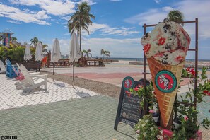 An ice cream cone with a sign, beach chairs, umbrellas, and palm trees.