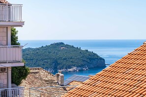 A coastal building with terracotta tiled roofs, a balcony, and a view of the sea and a forested island.
