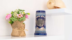 A small burlap basket with pink flowers and a blue decorative vase on a white shelf. - Andelic Sunset Apartments (Dubrovnik)