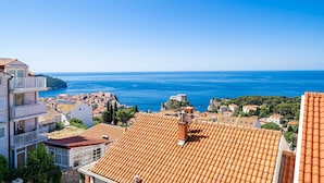 A coastal town with terracotta-roofed buildings, a clear blue sea, and a historic castle on a hill. - Andelic Sunset Apartments (Dubrovnik)