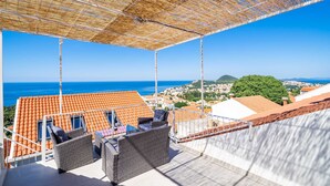 A balcony with wicker furniture, a view of the sea, and terracotta-roofed buildings in the background. - Andelic Sunset Apartments (Dubrovnik)