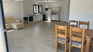 Un grand espace de vie comprenant une table à manger et des chaises, un canapé et, au fond, une cuisine.