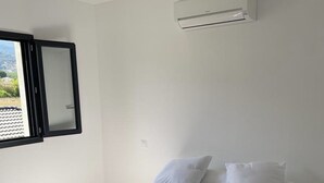 Une chambre à coucher avec un lit, du linge de lit blanc, une fenêtre donnant sur un paysage agréable et un appareil de climatisation.