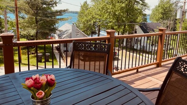 Ein Balkon mit Seeblick, einem Metallgeländer und einem Tisch mit Blumenvase.