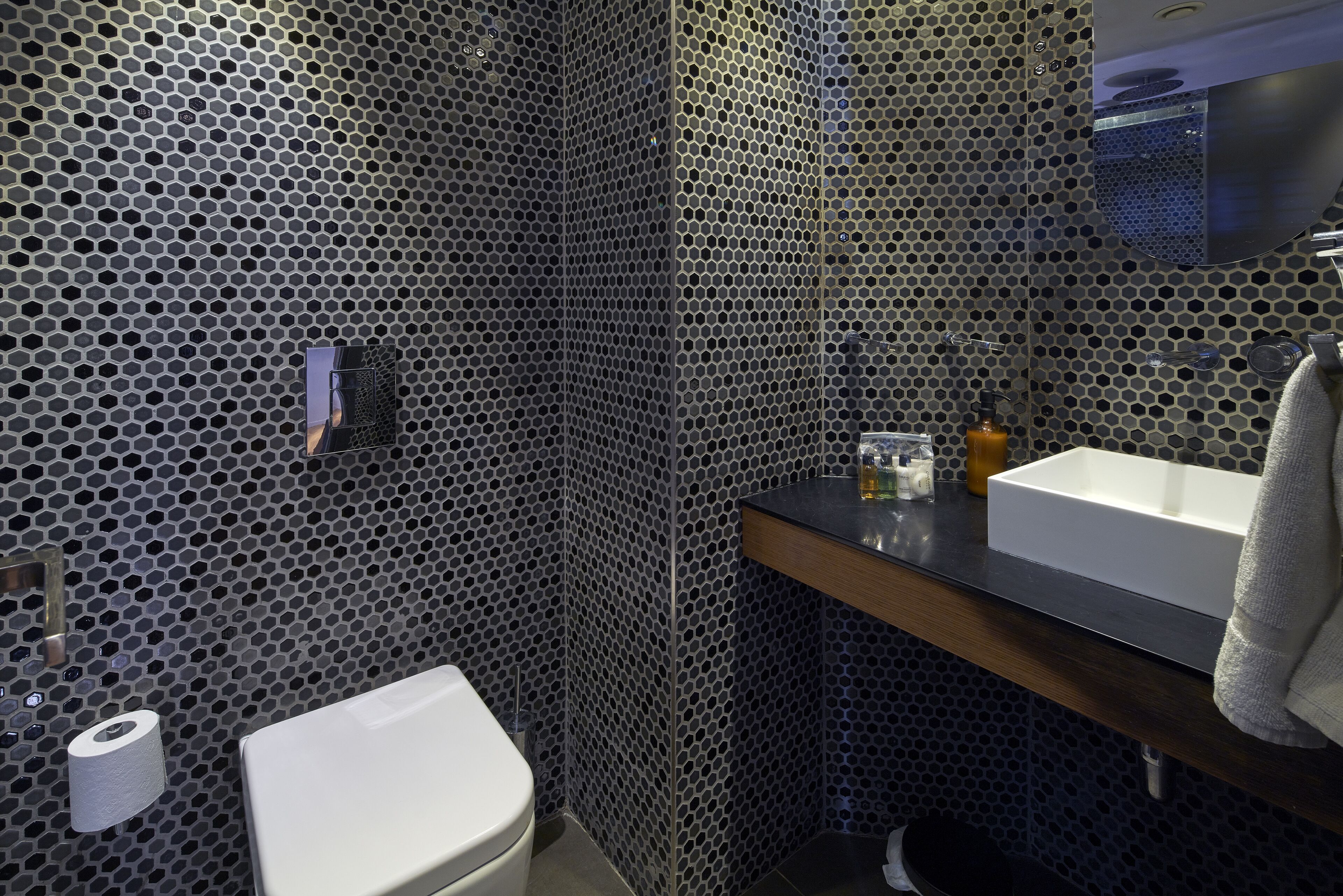 A bathroom with a perforated metal wall, a white toilet, a sink with a mirror, and a towel hanging on the wall.