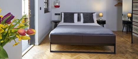 A modern bedroom with a bed, bedside tables, a hanging light fixture, and a wooden floor.