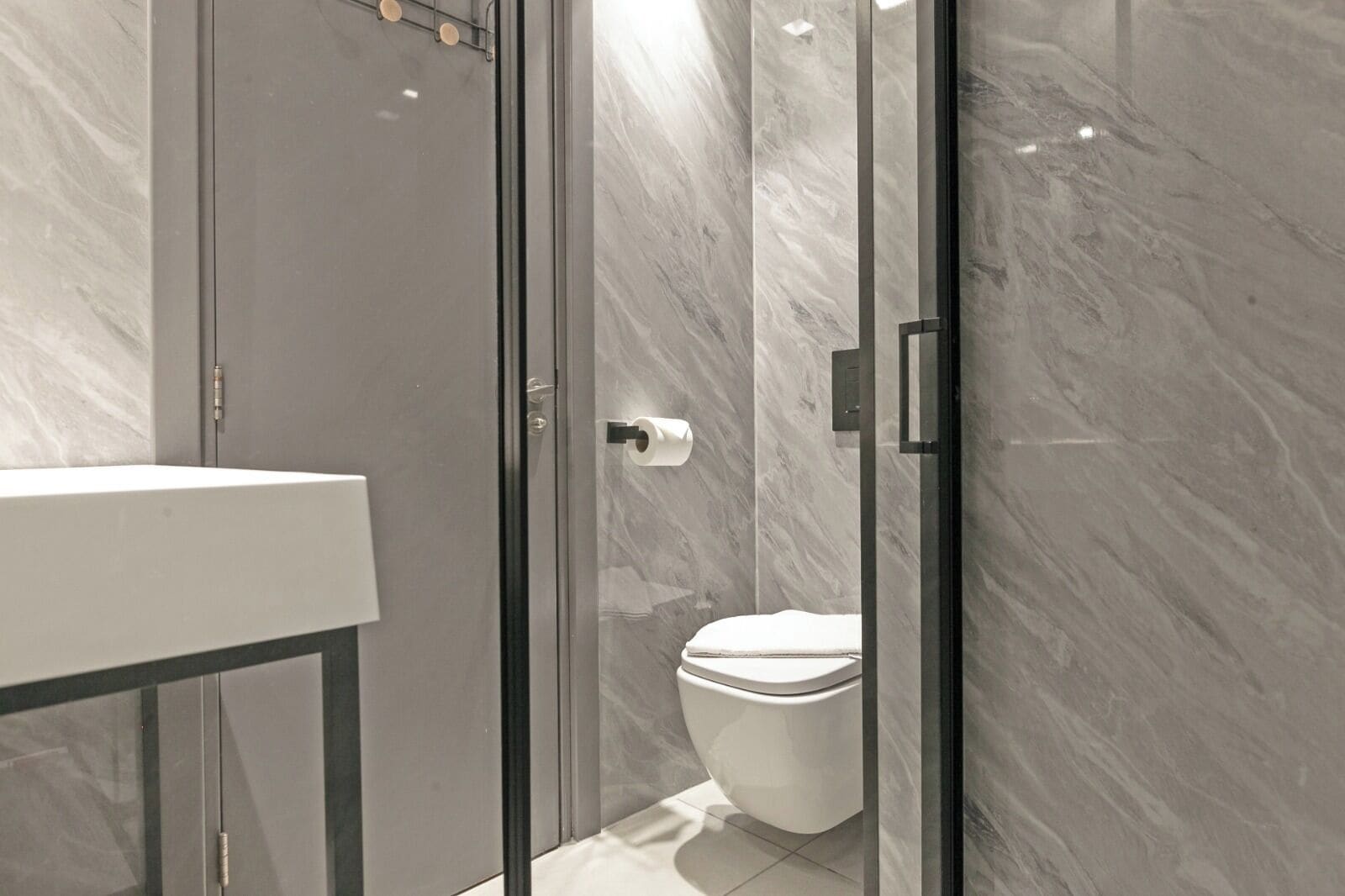A modern bathroom with a glass shower enclosure, a white toilet, and a marble wall.
