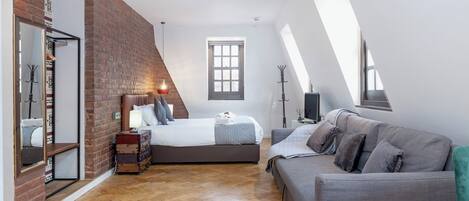 A modern loft bedroom with a loft bed, a gray sofa, and a brick accent wall.