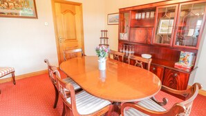 A dining room with a wooden table, chairs, a cabinet with glass doors, and a painting on the wall. - Braeside Farm House (Ballymena)