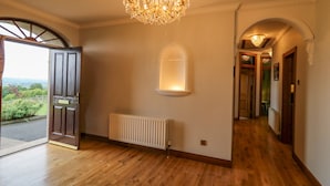 An interior hallway with wooden flooring, a chandelier, a radiator, and a door leading outside. - Braeside Farm House (Ballymena)