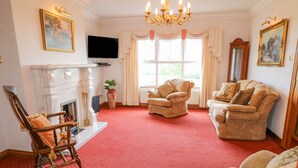 A spacious living room with a red carpet, a fireplace, and two armchairs. - Braeside Farm House (Ballymena)