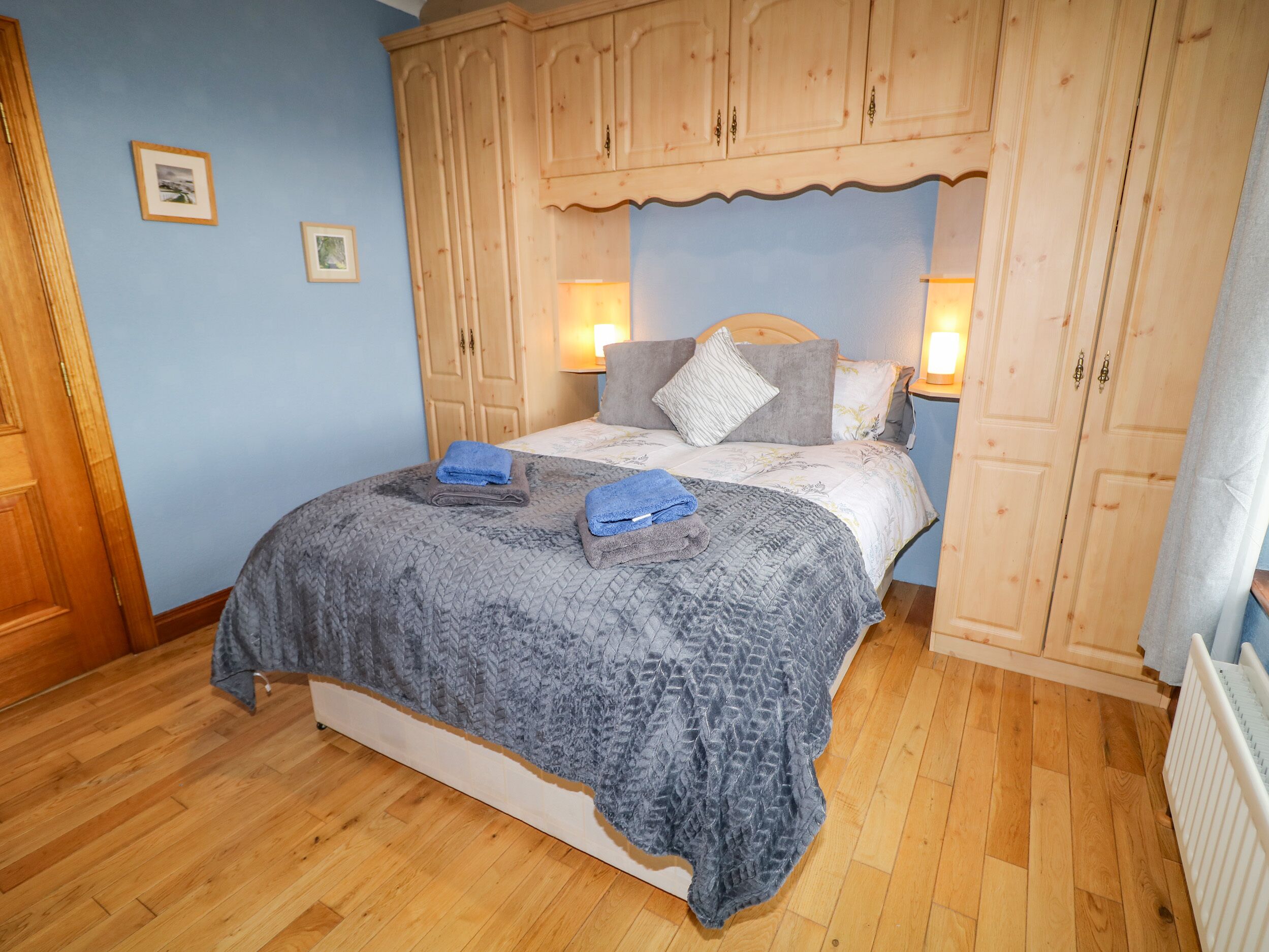 Un dormitorio con cama, armario de madera y dos lámparas fijadas a la pared.