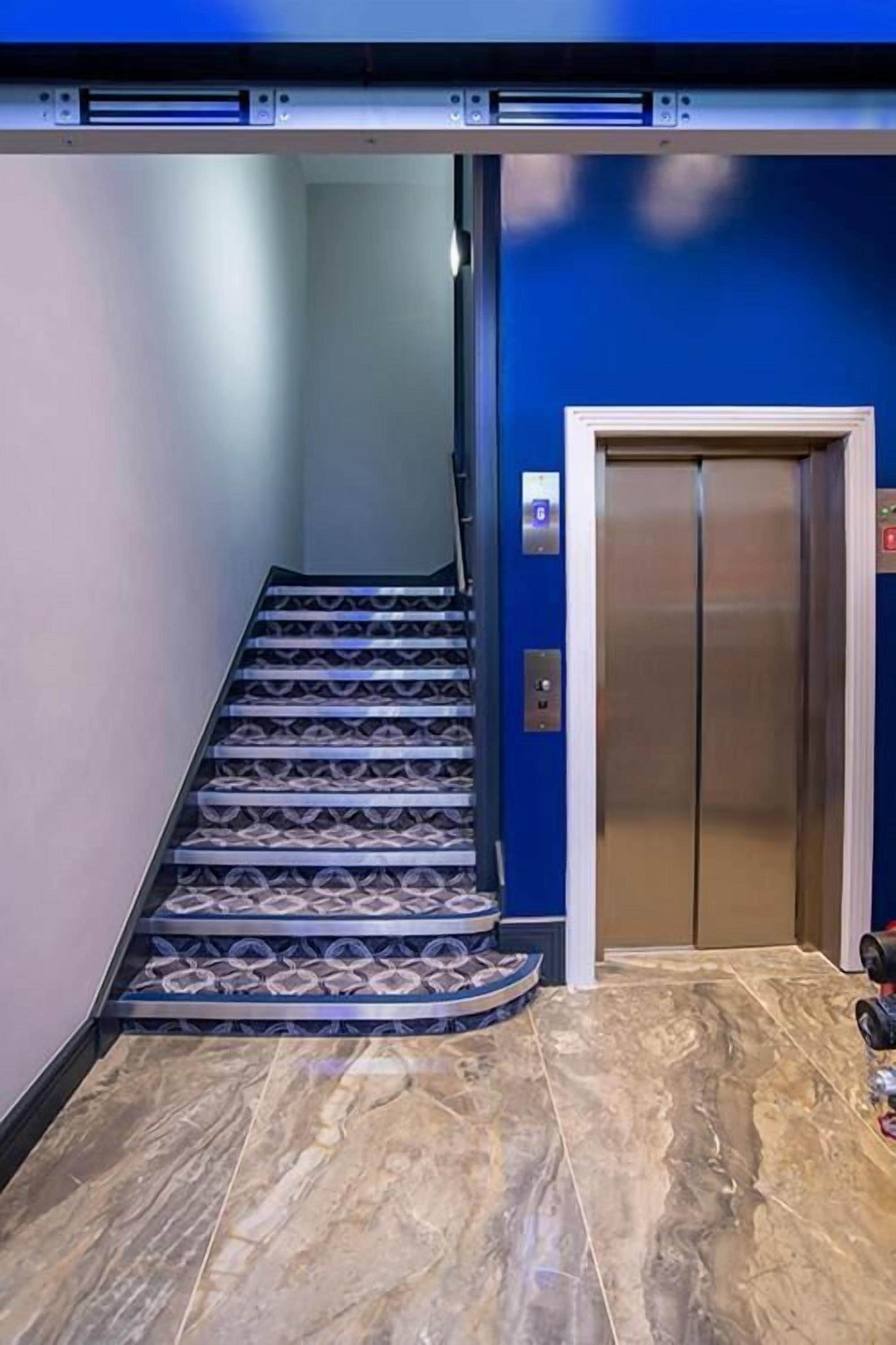 Passadís amb sòl de marbre que condueix a un ascensor, amb una paret d'accent blau.
