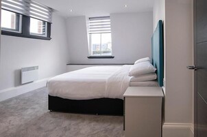 Un dormitorio con cama, mesita de noche, ventana y radiador.