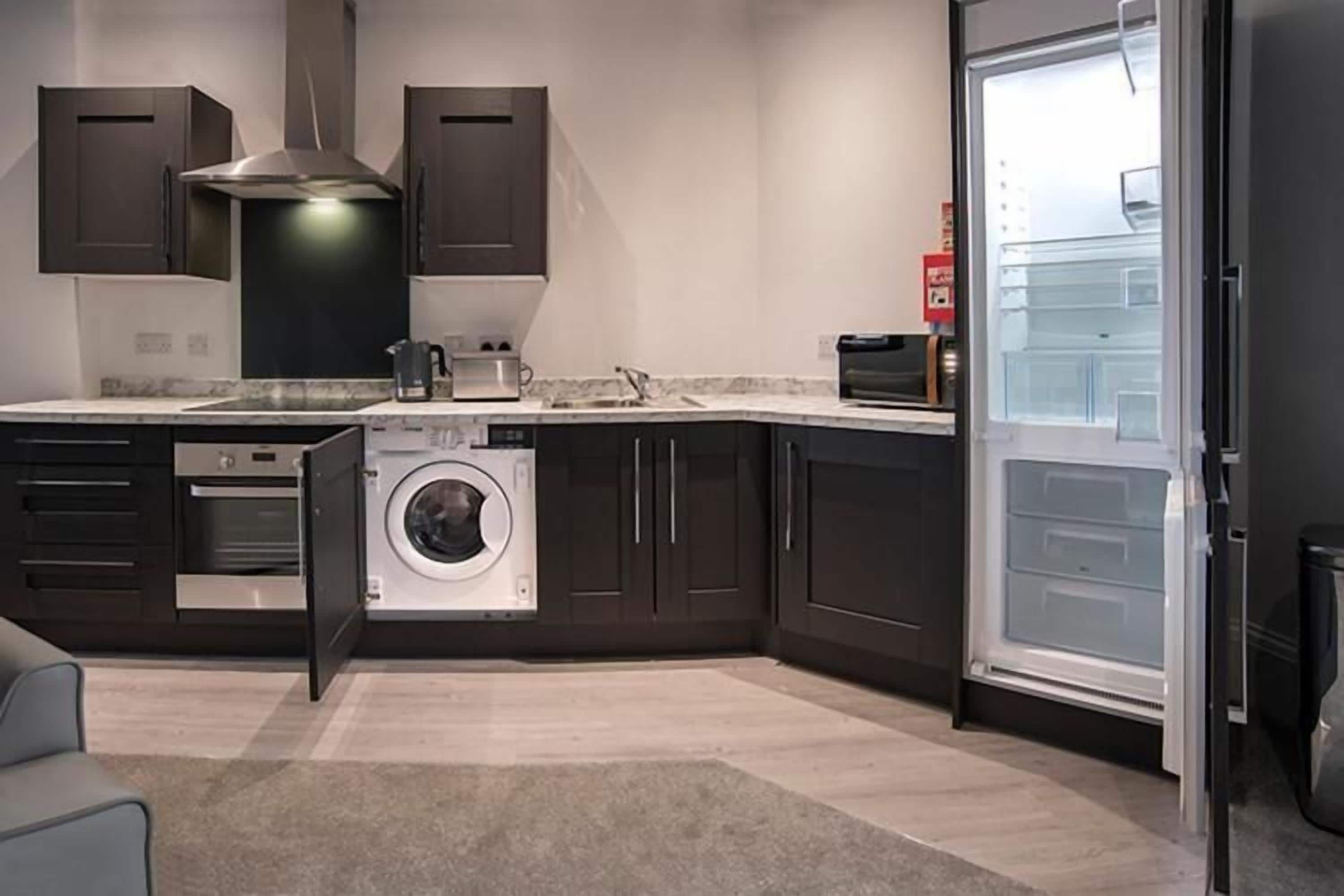 A compact kitchen with dark cabinets, a built-in washer, a microwave, and a refrigerator.