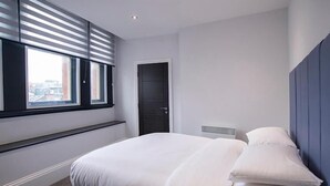 Een moderne slaapkamer met een groot bed, een raam met zonwering, een deur en een hoofdeinde.