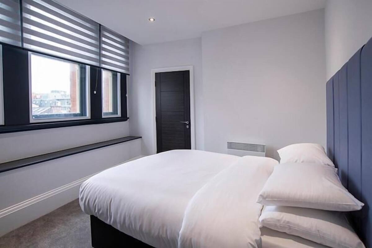 Ein modernes Schlafzimmer mit einem großen Bett, einem Fenster mit Jalousien, einer Tür und einem Kopfteil.