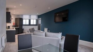 Een moderne woonkamer met een glazen salontafel, een witte bank en een flatscreen televisie aan de muur.