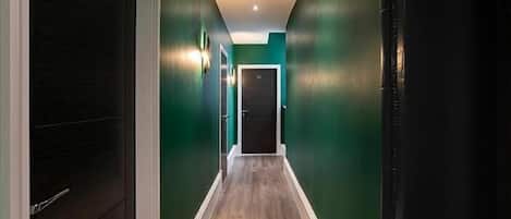 A hallway with dark wooden doors, green walls, and a wooden floor.