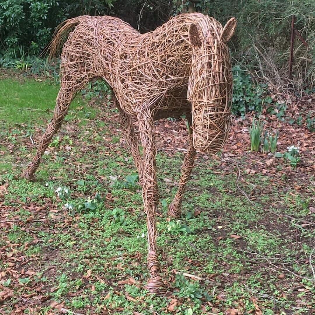 Een strooien sculptuur van een paard, in een natuurlijke omgeving met begroeiing en bomen op de achtergrond.