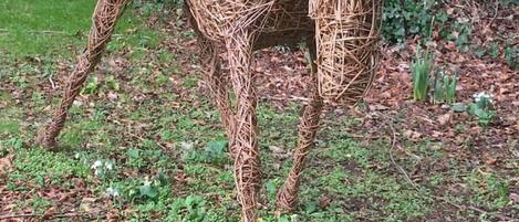 Een strooien sculptuur van een paard, in een natuurlijke omgeving met begroeiing en bomen op de achtergrond.