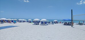 A beach with rows of blue chairs and white umbrellas, a volleyball net, and a sandy shore.