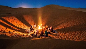 A group of people gathered around a campfire in a desert setting. - Camel Trek Bivouac in Merzouga (Taouz)