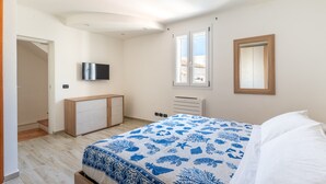 A bedroom with a bed, a TV mounted on the wall, a window, and a door leading to another room. - Aquamarine Terrace by Wonderful Italy (Siracusa)