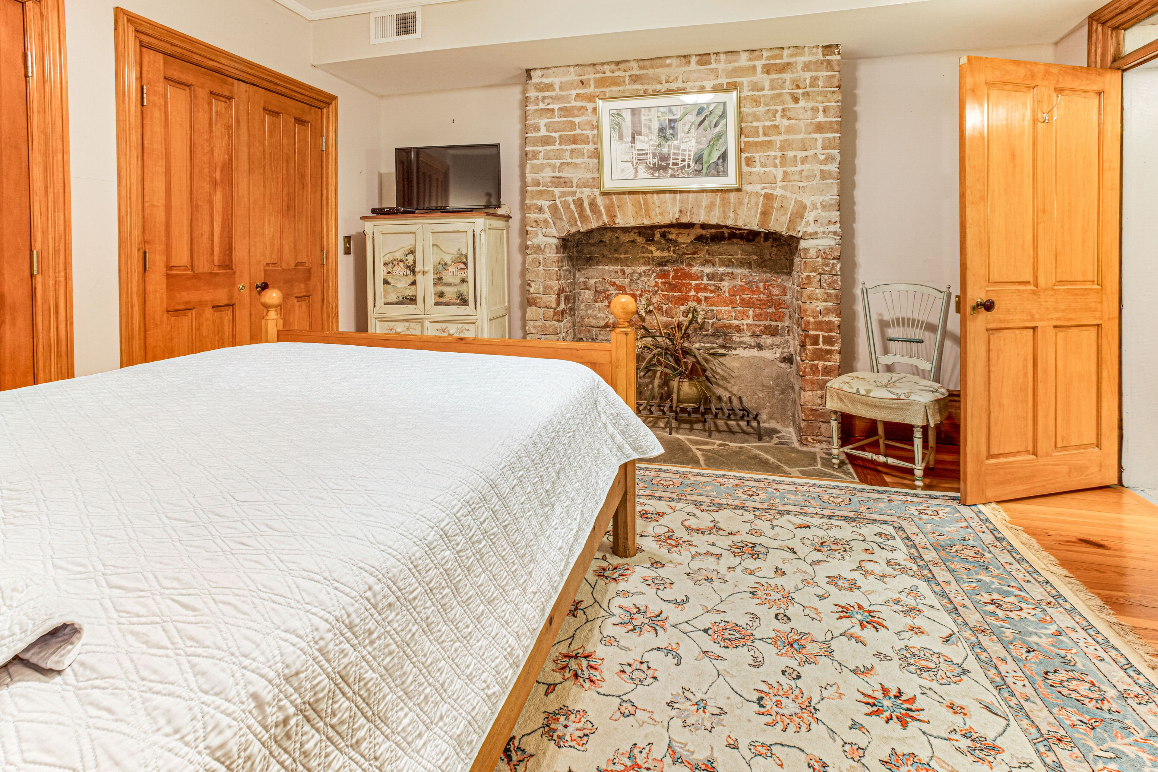 A bedroom with a bed, a fireplace, a wooden wardrobe, and a television on a cabinet.